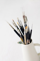 A set of paintbrushes in a white jug on a blank background.