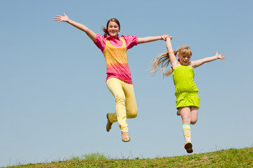 Two girls jumping on green meadow