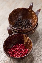pink and black peppercorns in coconut bowls on old wooden table