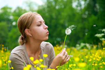 The girl blows on a dandelion on a background of a grass