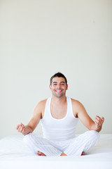 Smiling man sitting on bed meditating with copy-space