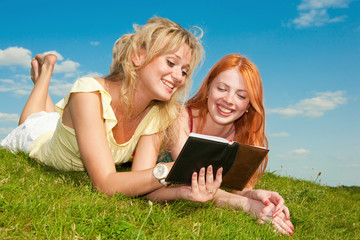 Two beautiful girls with notebooks outdoors. Lay on the green gr