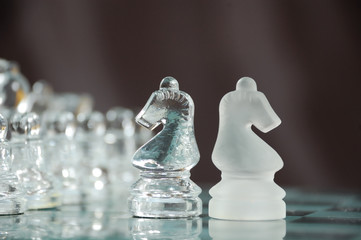 two glass knights on chessboard against black background