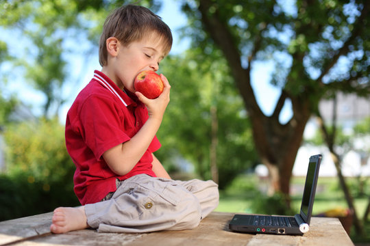 Boy eating apple with laptop
