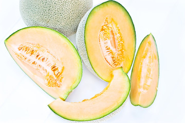 Whole cantaloupe and wedges on a white beadboard.