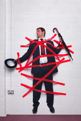 Businessman stuck to wall with red tape