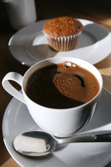 Fresh brewed cup of coffee and muffin on table in sunlight