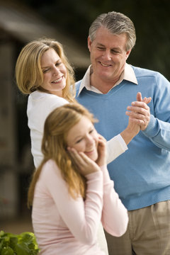 Mature couple dancing outdoors and looking at amused daughter
