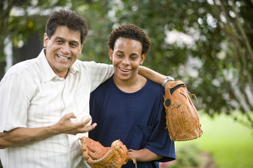 Interracial father and teenager in backyard with baseball gloves
