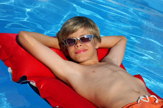 entspannter Junge auf Luftmatratze im Pool mit Sonnenbrille