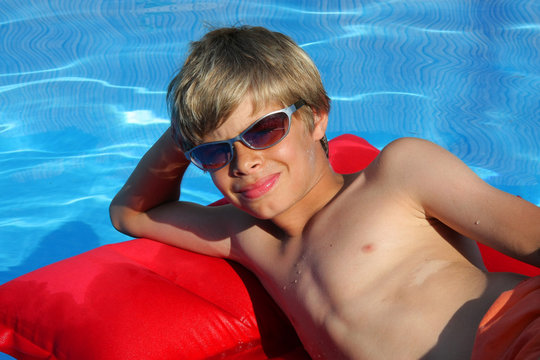 grinsender Junge auf Luftmatratze im Swimming Pool mit Brille