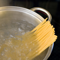 Spaghetti boiling in a metal pan with dark background