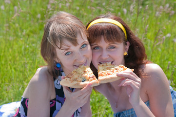 Two girls on a meadow eat a pizza