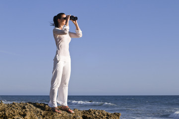 Frau mit Fernglas auf einem Felsen