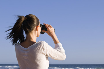 Frau mit Fernglas blickt auf das Meer
