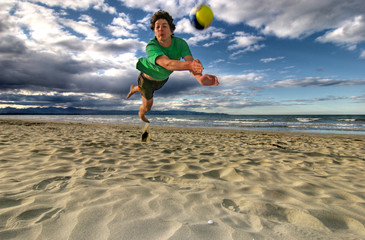 Man is jumping for a volleyball on a beach