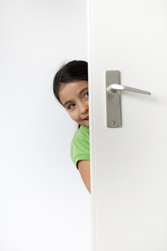Little girl is hiding behind a door