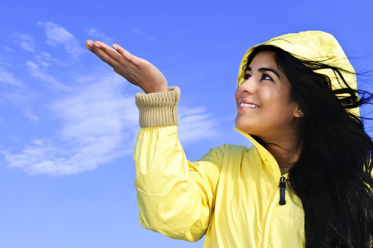 Beautiful young woman in raincoat checking for rain
