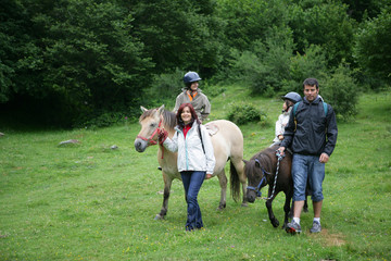 Homme et femme se promenant avec enfants assis sur poneys