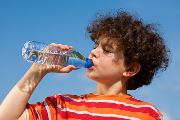 Boy drinking water against blue sky