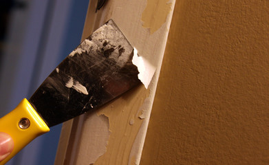 A close-up of a person stripping paint using a putty knife..