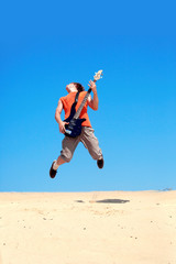 Young man with guitar jumping on a background of blue sky