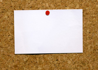 Small blank white business card attached to a cork notice board.
