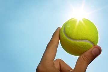 Hand holding tennis ball up to the sky