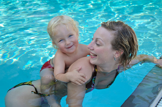 Glückliche junge Mutter mit Kind schwimmt im Pool