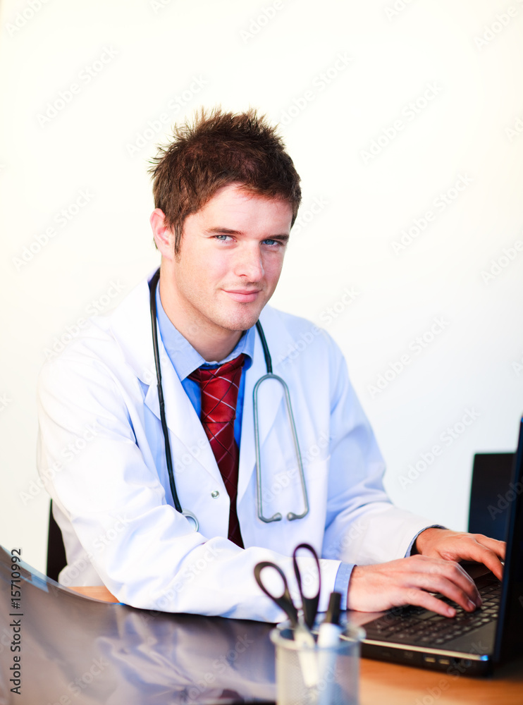 Wall mural smiling young doctor working on a computer