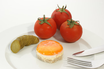 fried egg on a plate with tomato and gherkin