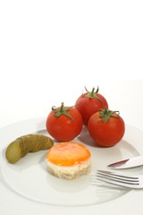fried egg on a plate with tomato and gherkin