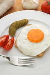 one fried egg on toast with tomato and gherkin