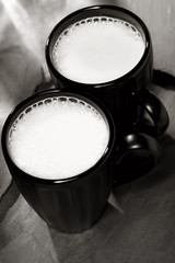 two mugs with milk on black backdrop