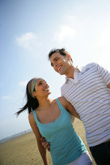 homme et femme souriants en se baladant à la plage