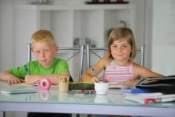 deux enfants souriants assis à un bureau faisant leurs devoirs
