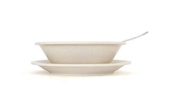 Plain beige soup plate with spoon and saucer side view isolated