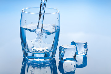 water splashing into glass with ice cubes