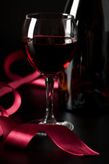glass of red wine and red ribbon over black background