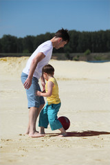 father with son play football on sand