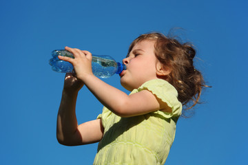 girl drinks water from  plastic bottle against blue sky