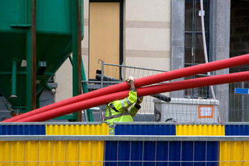 Worker at a construction site carrying red pipes.