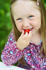 Smiling little girl eating a strawberry.