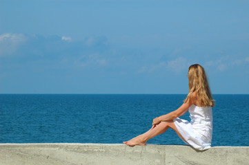The woman sits and looks at the sea