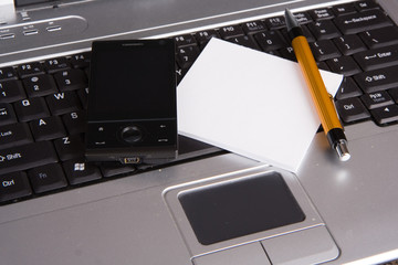Smart phone, note pad and a pen on a laptop