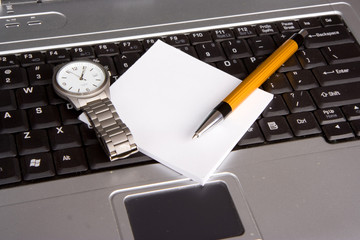Pen, note pad and a watch on laptop keyboard