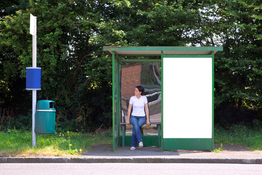 Woman Sat At A Bus Stop Next To Blank Billboard