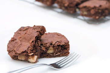 Two freshly baked brownies on white with a fork