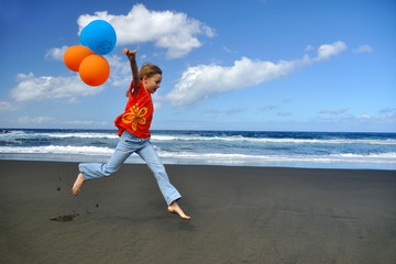 Fillette jouant sur une plage de sable noir avec des ballons.