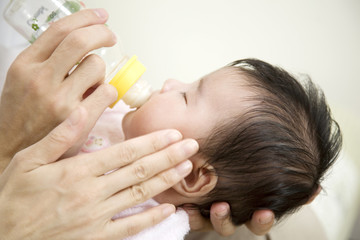 ミルクを飲む赤ちゃんと両親の手